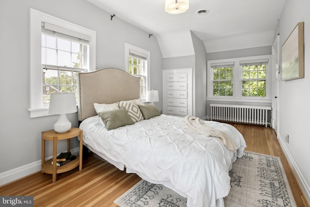 bedroom featuring hardwood / wood-style flooring, vaulted ceiling, and radiator