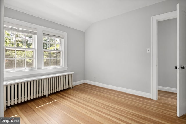 spare room featuring vaulted ceiling, radiator, and light wood-type flooring