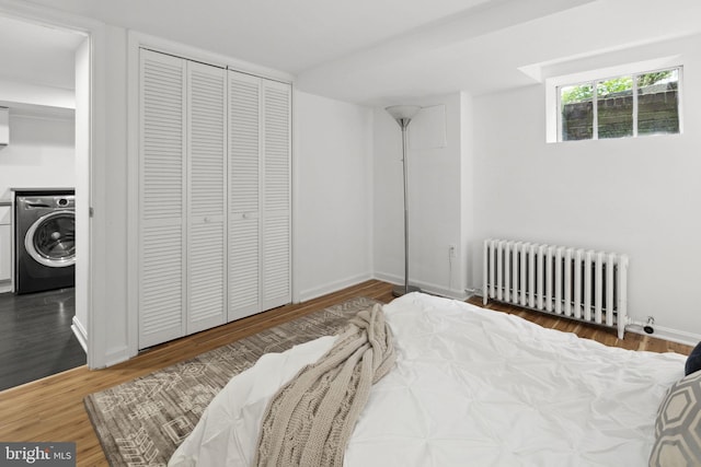 bedroom with hardwood / wood-style flooring, radiator heating unit, washer / clothes dryer, and a closet