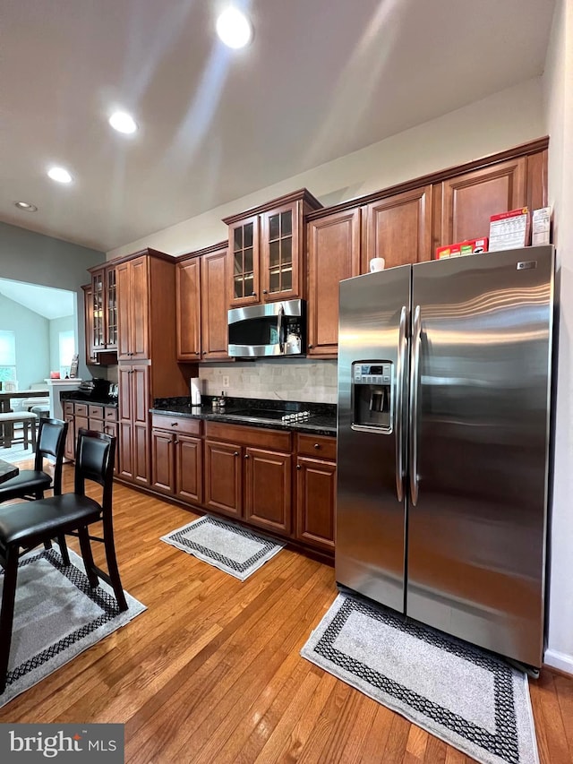 kitchen featuring stainless steel appliances, light hardwood / wood-style floors, decorative backsplash, and dark stone counters