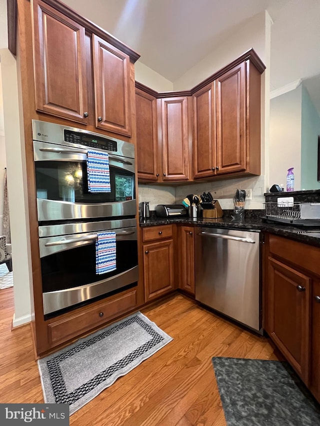 kitchen with stainless steel appliances, dark stone countertops, and light wood-type flooring