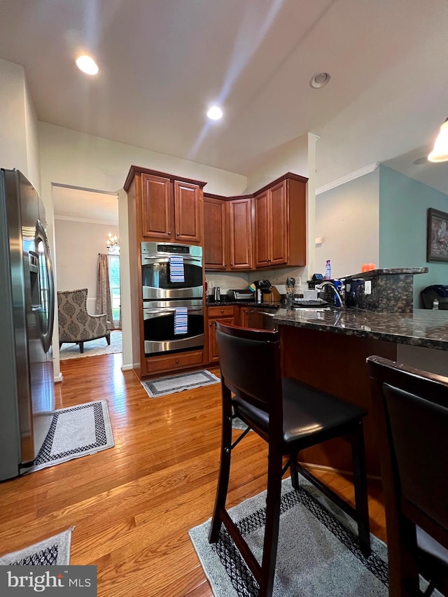 kitchen with appliances with stainless steel finishes, sink, light hardwood / wood-style flooring, and dark stone counters