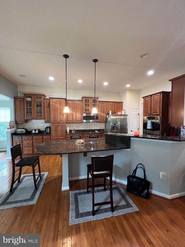 kitchen featuring decorative light fixtures, backsplash, a kitchen bar, stainless steel appliances, and dark wood-type flooring