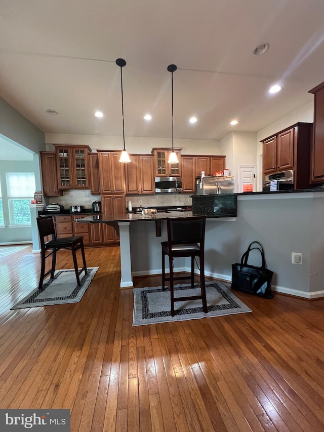 kitchen featuring stainless steel appliances, pendant lighting, dark wood-type flooring, and a breakfast bar area