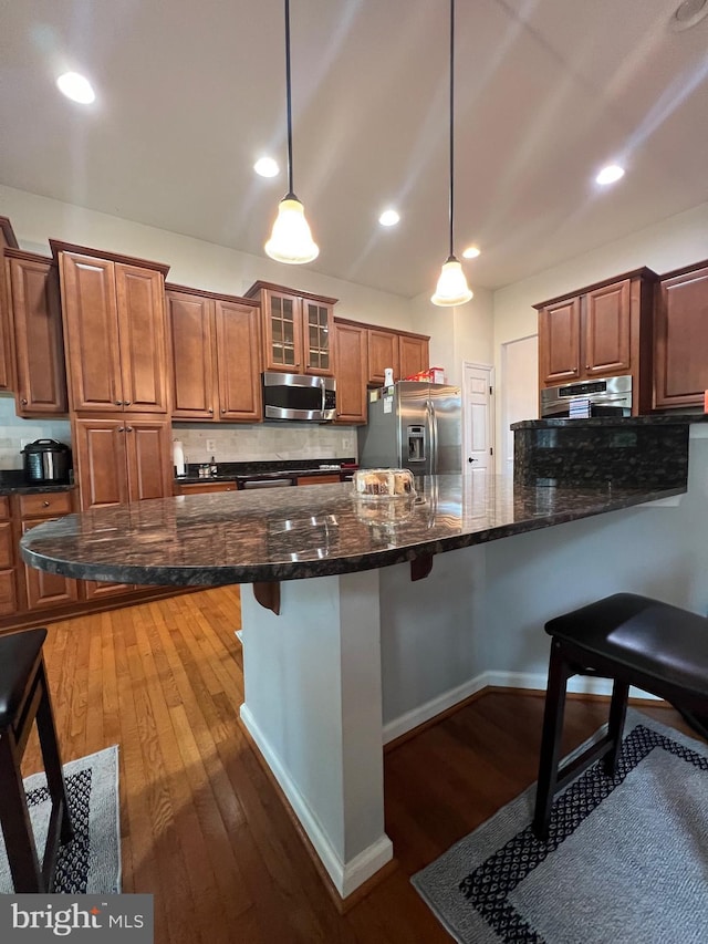 kitchen with appliances with stainless steel finishes, a breakfast bar, hanging light fixtures, and dark stone counters