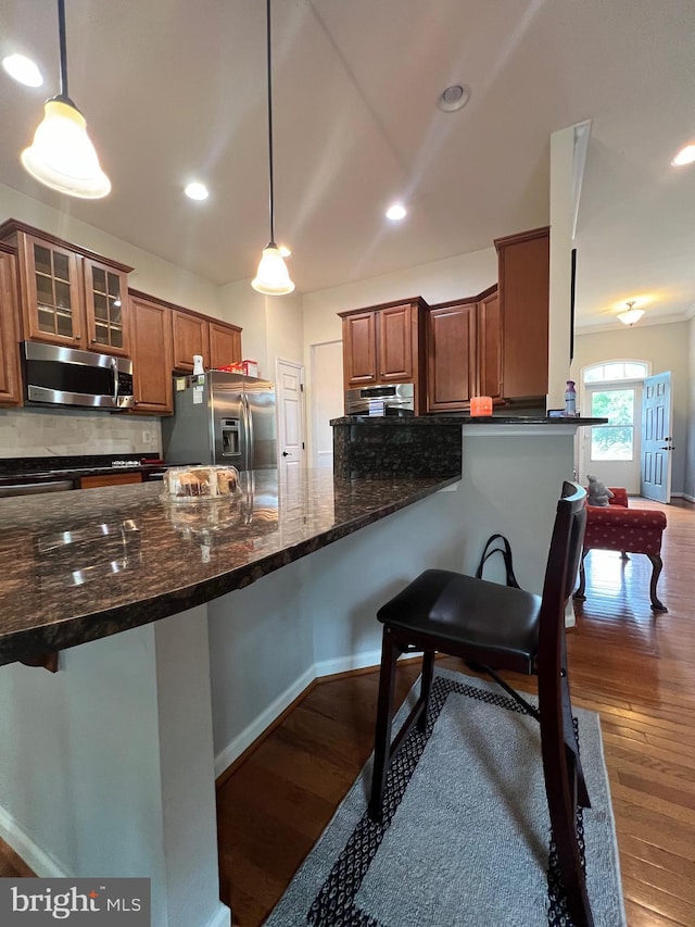 kitchen featuring dark stone countertops, hanging light fixtures, a kitchen bar, and appliances with stainless steel finishes