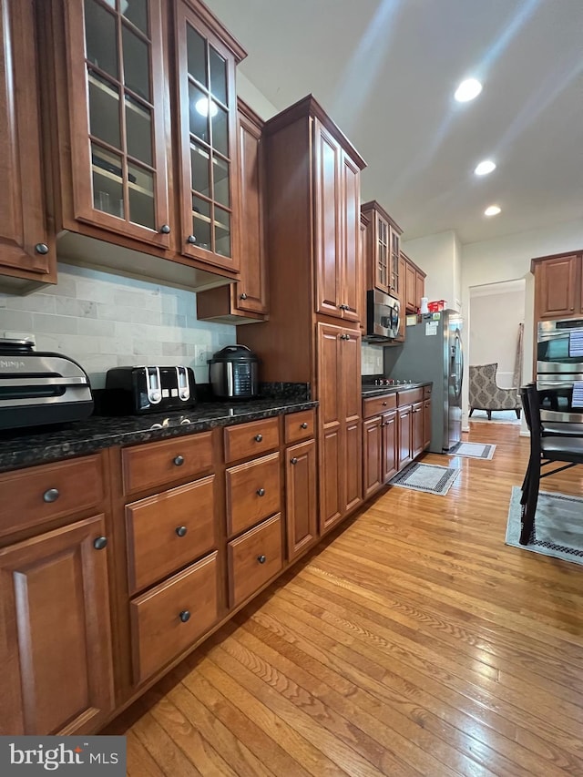 kitchen featuring appliances with stainless steel finishes, light hardwood / wood-style floors, decorative backsplash, and dark stone counters