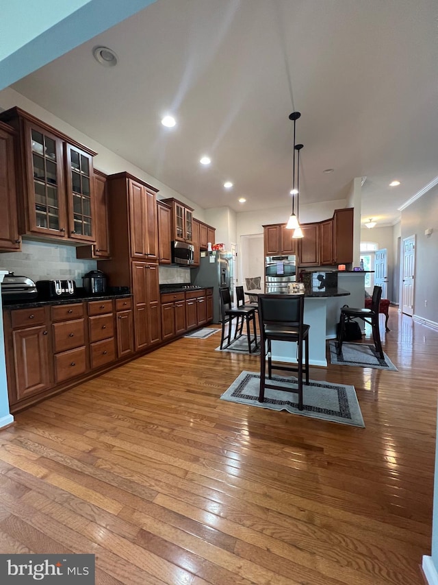 kitchen with appliances with stainless steel finishes, backsplash, a kitchen bar, and decorative light fixtures