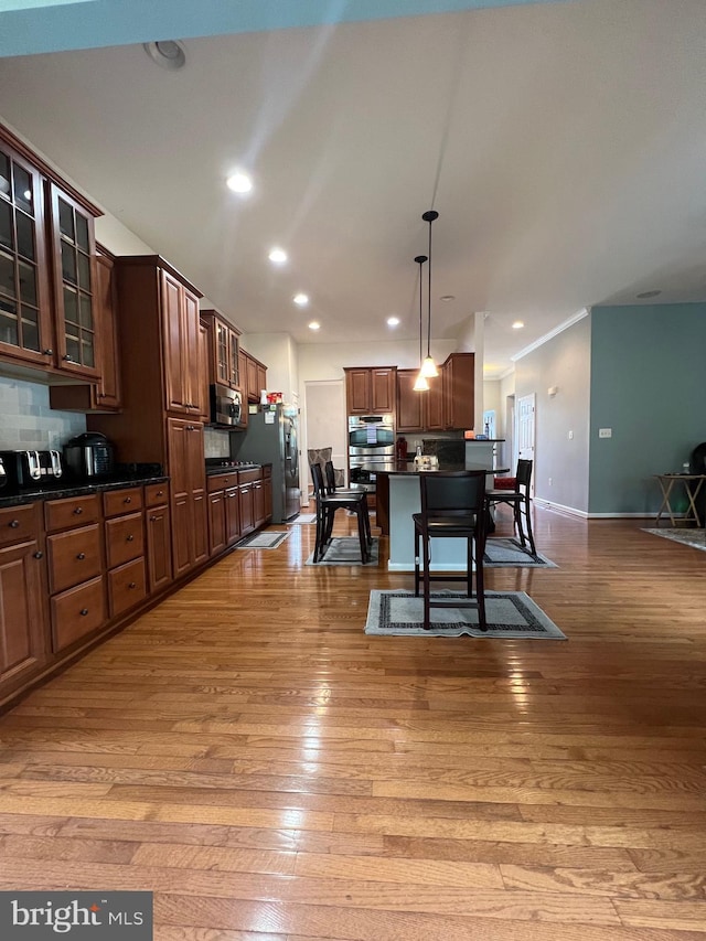 kitchen with appliances with stainless steel finishes, a kitchen island, hanging light fixtures, and light hardwood / wood-style flooring