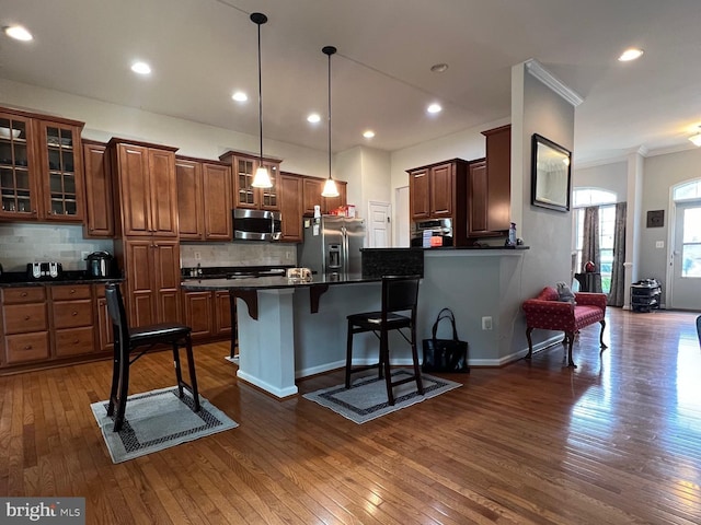 kitchen with pendant lighting, a breakfast bar area, backsplash, stainless steel appliances, and dark hardwood / wood-style flooring