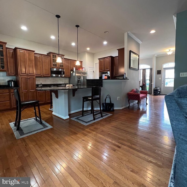 kitchen with dark wood-type flooring, stainless steel appliances, a kitchen breakfast bar, and decorative light fixtures