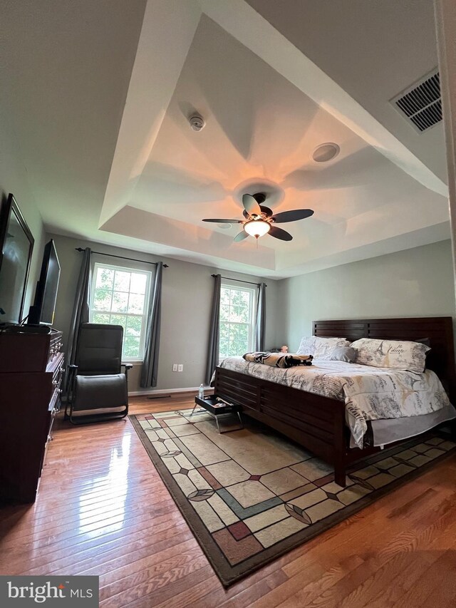 bedroom featuring ceiling fan, a raised ceiling, and light hardwood / wood-style flooring