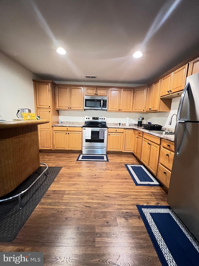 kitchen with stainless steel appliances, light brown cabinetry, and light hardwood / wood-style flooring