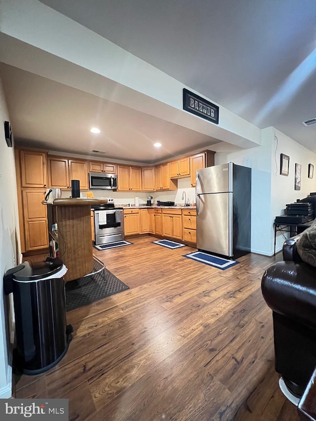 kitchen with light brown cabinetry, wood-type flooring, and stainless steel appliances