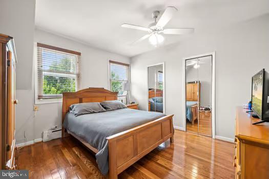 bedroom with a baseboard radiator, a closet, hardwood / wood-style flooring, and ceiling fan