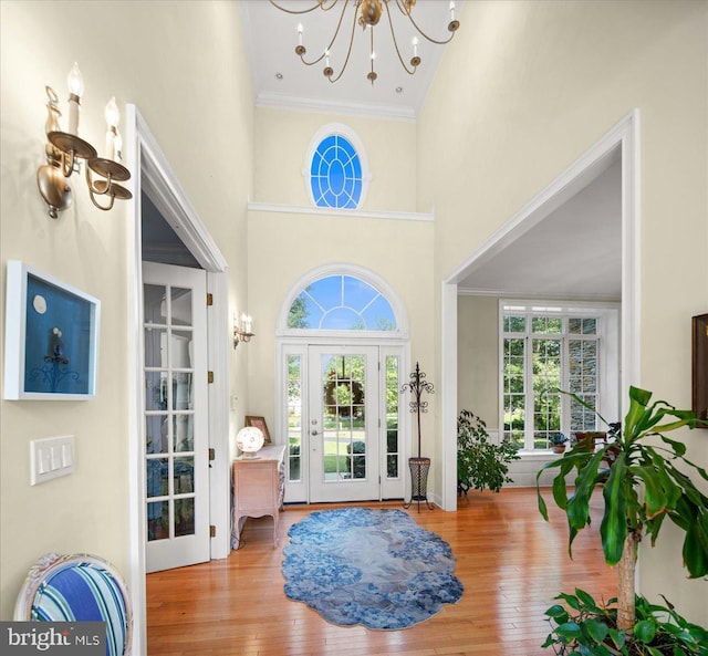 foyer featuring ornamental molding, light hardwood / wood-style flooring, a chandelier, and a towering ceiling