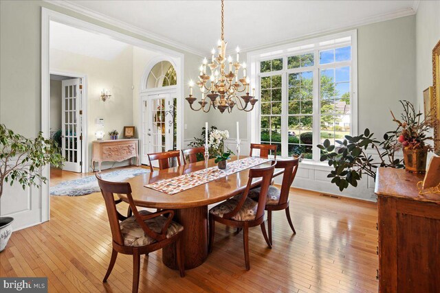 dining area with light hardwood / wood-style floors, ornamental molding, french doors, and a chandelier