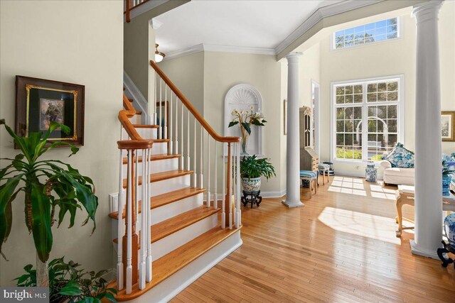 foyer entrance with light hardwood / wood-style flooring, crown molding, and ornate columns