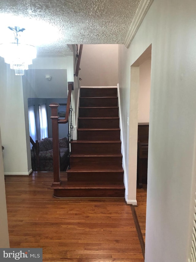 stairs featuring a textured ceiling, wood-type flooring, and a chandelier