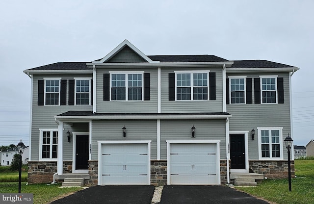 multi unit property with driveway, stone siding, and a garage