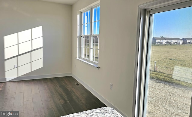 empty room featuring a healthy amount of sunlight, baseboards, visible vents, and dark wood-style flooring