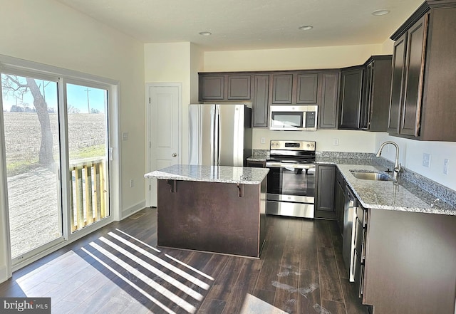 kitchen with light stone counters, sink, stainless steel appliances, and a center island