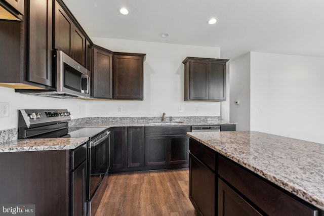 kitchen featuring dark brown cabinetry, appliances with stainless steel finishes, wood finished floors, light stone countertops, and a sink