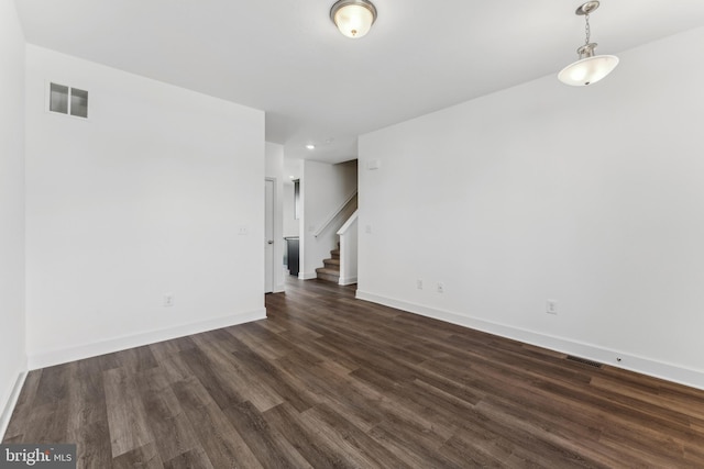 empty room with dark wood-style flooring, visible vents, stairway, and baseboards