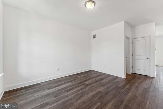 unfurnished room featuring dark wood-type flooring, visible vents, and baseboards