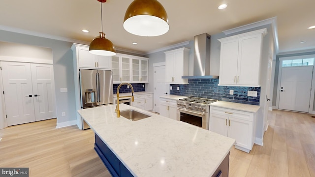 kitchen with pendant lighting, wall chimney range hood, white cabinetry, premium appliances, and ornamental molding