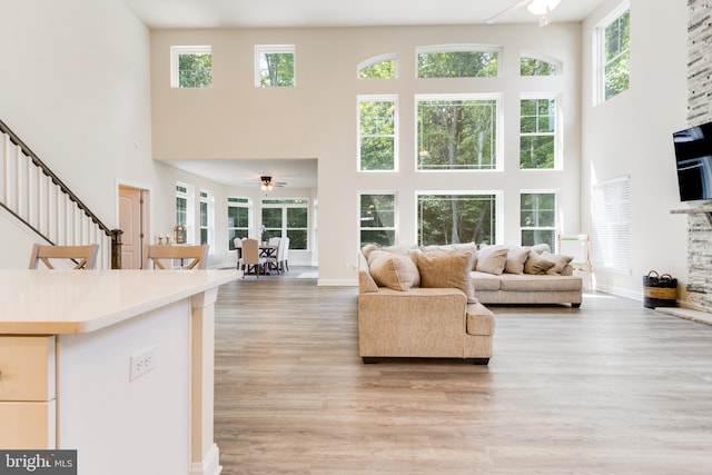 living room featuring light hardwood / wood-style flooring, ceiling fan, and a towering ceiling