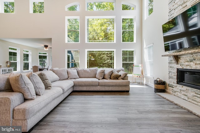 living room featuring a stone fireplace, ceiling fan, hardwood / wood-style flooring, and a high ceiling