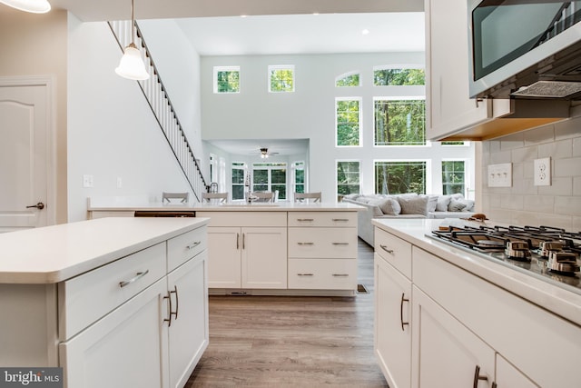 kitchen featuring tasteful backsplash, stainless steel appliances, pendant lighting, light hardwood / wood-style floors, and white cabinetry