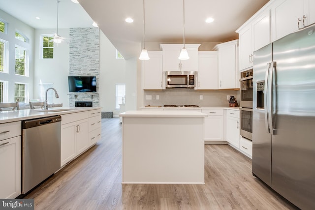 kitchen with a center island, pendant lighting, stainless steel appliances, light hardwood / wood-style floors, and a fireplace