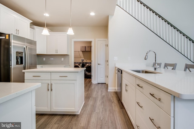 kitchen featuring appliances with stainless steel finishes, light hardwood / wood-style flooring, sink, hanging light fixtures, and backsplash