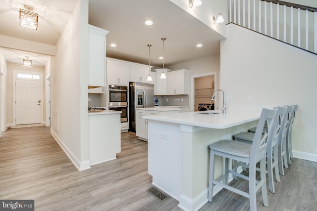 kitchen with stainless steel appliances, sink, decorative light fixtures, light wood-type flooring, and white cabinetry