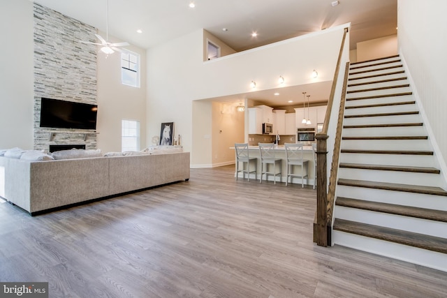 unfurnished living room featuring ceiling fan, a stone fireplace, light wood-type flooring, and a towering ceiling