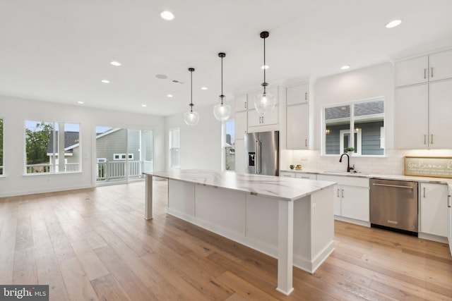 kitchen with white cabinetry, hanging light fixtures, a center island, light stone counters, and stainless steel appliances