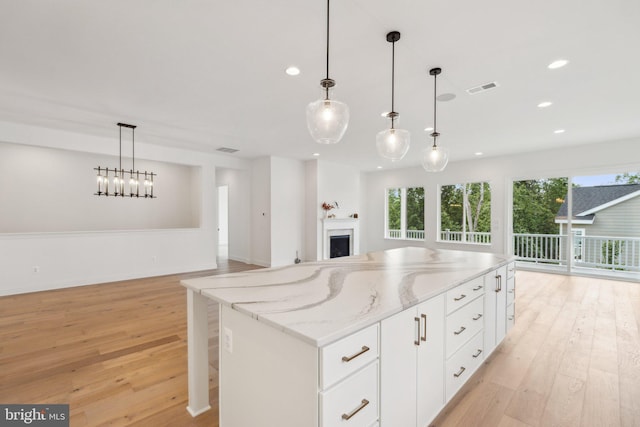 kitchen with decorative light fixtures, white cabinets, a center island, light stone countertops, and light wood-type flooring