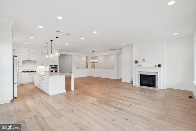 kitchen featuring stainless steel appliances, a fireplace with flush hearth, light wood-style floors, white cabinets, and light countertops