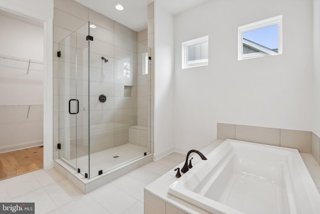 full bath featuring a stall shower, tile patterned flooring, a spacious closet, and a garden tub