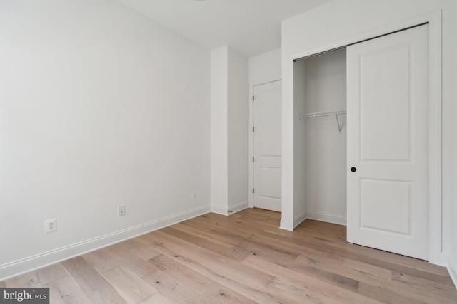 unfurnished bedroom featuring light wood-style floors, a closet, and baseboards