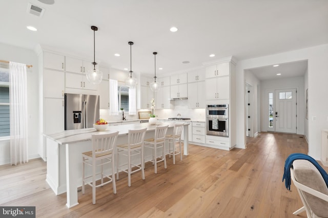 kitchen featuring a kitchen island, decorative light fixtures, white cabinets, stainless steel appliances, and light hardwood / wood-style flooring