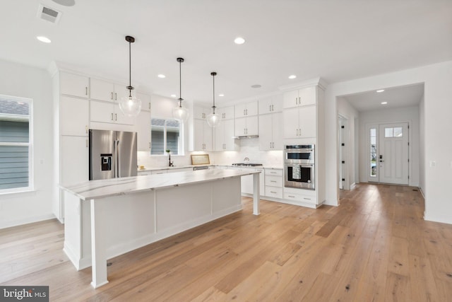 kitchen with white cabinetry, stainless steel appliances, decorative light fixtures, and a center island