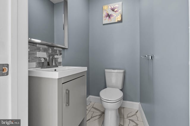 half bathroom featuring baseboards, toilet, marble finish floor, vanity, and backsplash