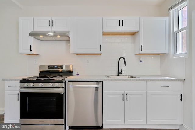 kitchen with stainless steel appliances, white cabinets, wall chimney range hood, sink, and decorative backsplash