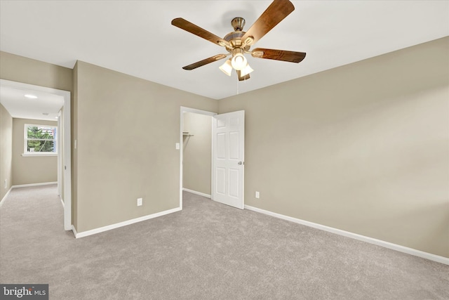 unfurnished bedroom with ceiling fan, a closet, light carpet, and a walk in closet