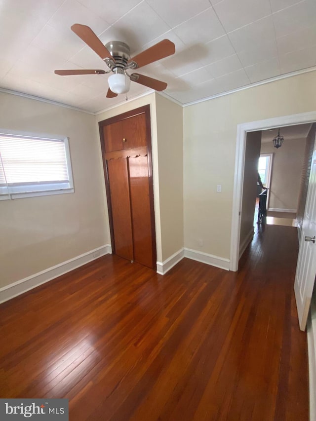 unfurnished bedroom featuring ceiling fan, dark wood-type flooring, a closet, and ornamental molding