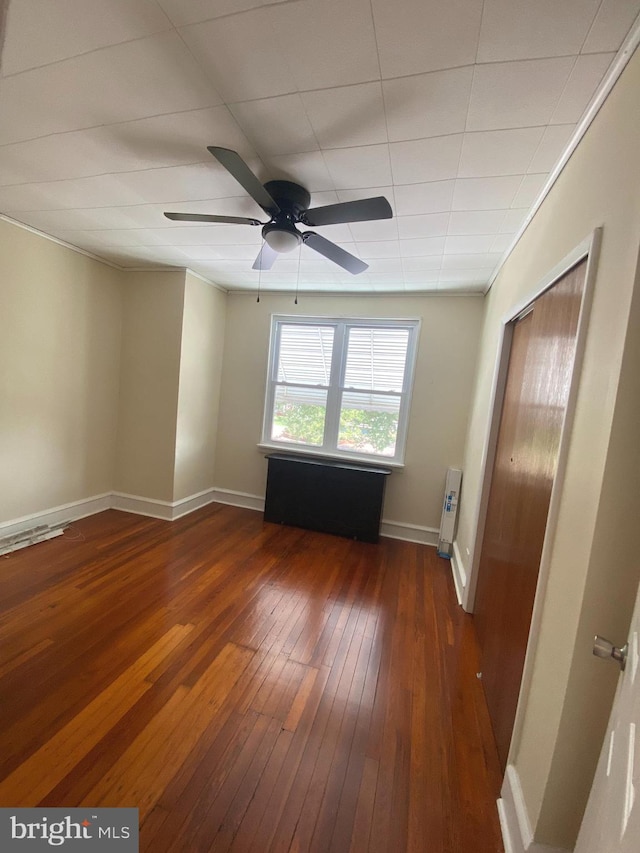 empty room with radiator, dark hardwood / wood-style flooring, ornamental molding, and ceiling fan