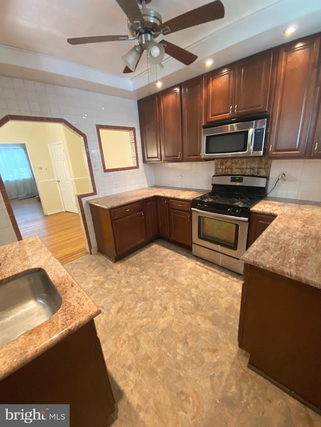 kitchen featuring light hardwood / wood-style flooring, ceiling fan, appliances with stainless steel finishes, decorative backsplash, and sink